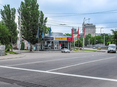 View of a car dealership featuring Chevrolet, Opel, and Kia brands at a city intersection. Urban road with traffic and industrial buildings in the background. Zaporizhzhia, Ukraine - June 24, 2017