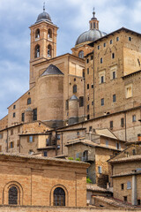 Obraz premium Historic red-brown brick houses of the old town with the Urbino Cathedral (Duomo of Urbino) visible in the distance. Urbino, Marche, Italy.