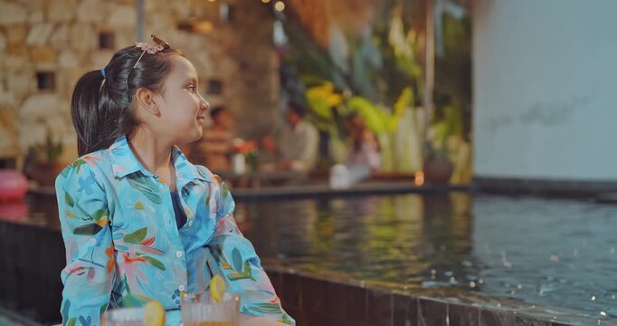 Indian happy relax girl sitting on water pool edge eat healthy grapes have fun joy outdoor villa house. Teen cute child kid enjoy picnic trip outside home place  
