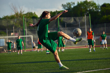Naklejka premium Teenage female soccer player jumping to kick ball during outdoor match. Concept of women football, match action, youth sport, resilience and active lifestyle.