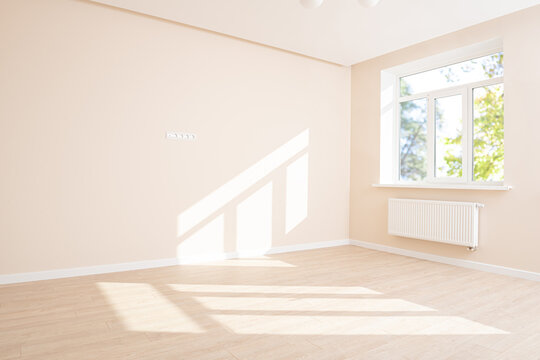 Empty room interior in light pastel colors with beige wall, wooden texture laminate floor and sunlight through white window