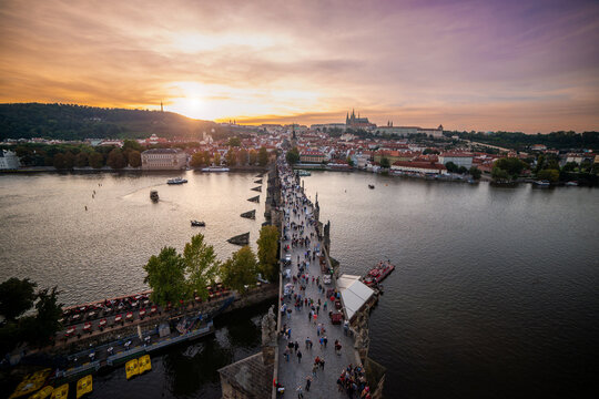 People walk Charles Bridge Prague at golden hour