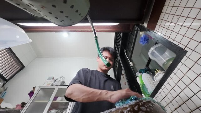Person scrubbing a soapy pot at a kitchen sink, viewed from a low angle indoors