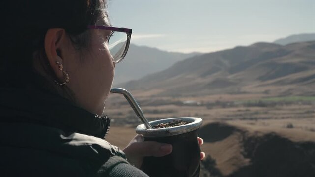 Close-up Profile of Woman Holding Traditional Yerba Mate Gourd and Bombilla Straw Against Andean Mountain Valley Landscape