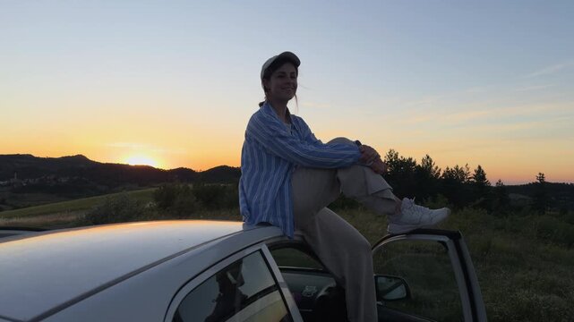 Beautiful young woman with a baseball cap smiling and posing at sunset. Gorgeous landscape with rolling hills and a warm orange sky