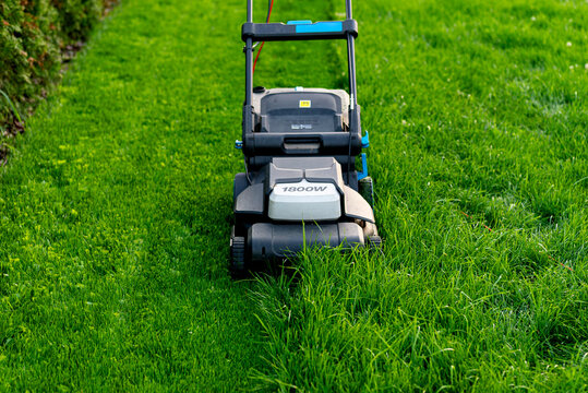 Electric lawn mower cutting tall overgrown grass