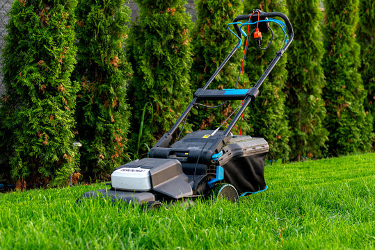 Electric lawn mower cutting overgrown lawn grass