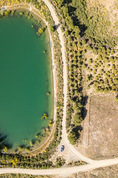 Aerial view of a turquoise reservoir bordered by a dirt road and pine trees in the arid landscape of Juviles, Andalusia, Spain.