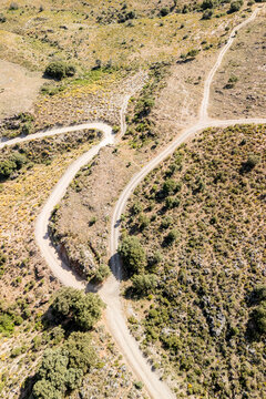 Aerial view of a winding dirt road intersection surrounded by arid hills, scattered trees, and shrubs in the rural landscape of Juviles, Andalusia, Spain.