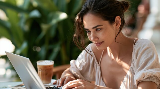 Young woman using her laptop in a comfortable cafe filled with vibrant plants while enjoying a cool beverage