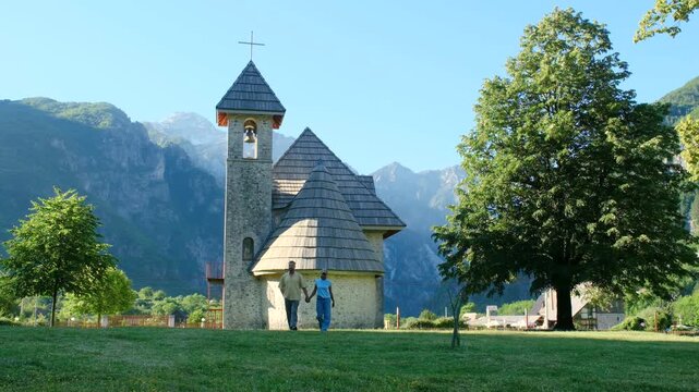 Albania captivates visitors with its stunning mountains and tranquil churches. A couple experiences the beauty of a peaceful afternoon as travelers admire a quaint church set against mountains