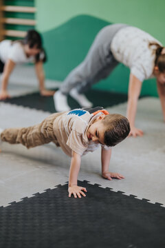 A young boy performs a push-up while other children follow along in a class. Group of kids exercising on foam mats in a playful gym setting.