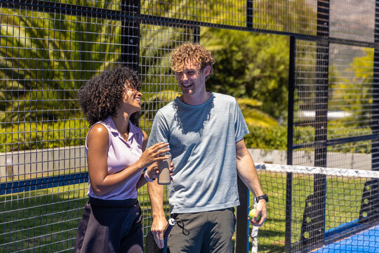 Couple standing on fenced blue sports court holding yellow ball and textured bottle with paddle