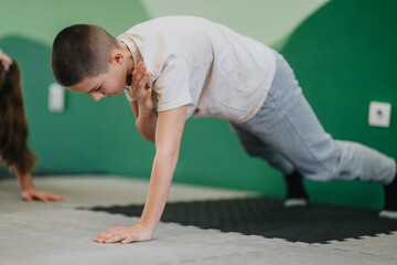 Fototapeta premium A boy performs a push-up on a gym mat while participating in a kids fitness activity. Another child practices beside him in a focused group exercise setting.