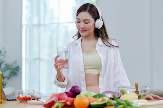 Asian women in good spirits hold glass clean water drink while cooking refresh themselves and ensure they have enough water which helps keep their bodies refreshed energetic beneficial health.