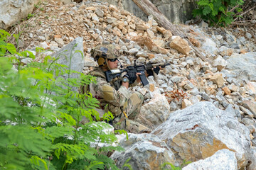 Fototapeta premium Male soldier in camouflage uniform sits on a rock on the edge high cliff in a mountainous area closely monitoring the border security situation. 