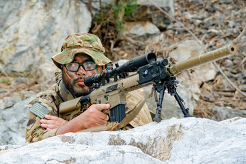 Fototapeta premium Snipers in camouflage uniforms conceal themselves behind rocks their rifles ready to fire at the enemy during combat.