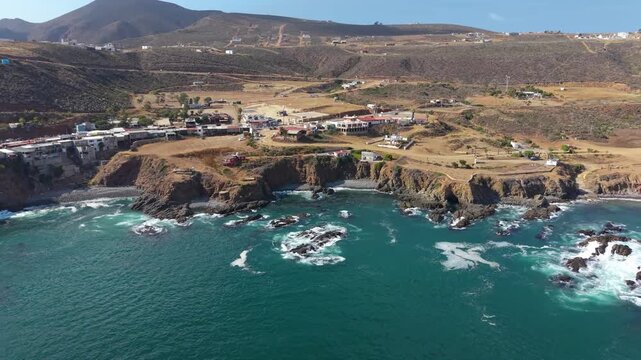 Aerial drone view of a small coastal village on a rocky bluff above turquoise water in Baja California.