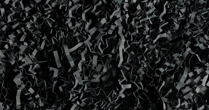 Black shredded paper. Close-up of dense black cut and crumpled paper strips forming chaotic layered texture. Smooth continuous rotation reveals dynamic shifts in light and deep shadows.