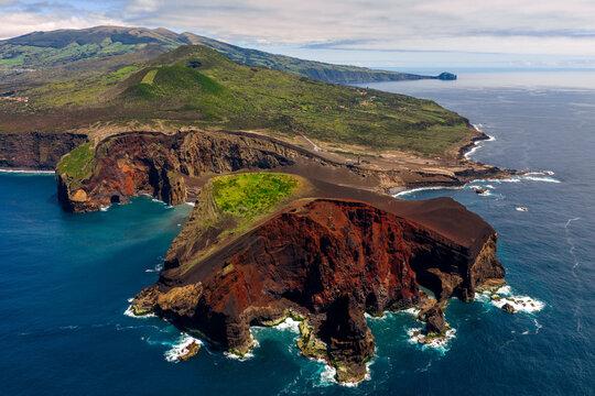 Aerial view of the Capelinhos volcano, showcasing its dramatic red and black volcanic cliffs, rugged coastline, and lush green landscape in Capelo, Azores, Portugal.