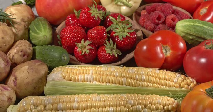 Various fresh healthy products on a gray table. Close-up footage of  corn, strawberries, cucumbers, tomatoes, green onions, potatoes, raspberries, dill, sweet peppers on a rotating table.