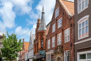 Fototapeta premium Historic brick houses and richly decorated facades line a picturesque street in the old town of Tønder beneath a blue sky with white clouds.