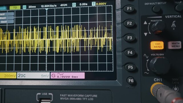 An engineer's hand adjusts the vertical scale on a digital oscilloscope, analyzing a complex yellow electrical signal. Concept of scientific research, diagnostics, and engineering.