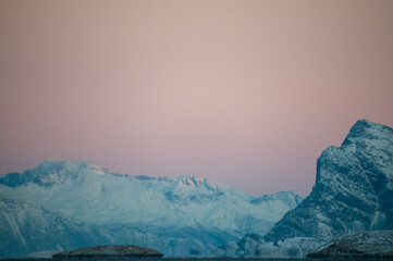 Obraz premium Landscape shot highlighting the rugged mountains and snow-covered beaches of arctic norway during a brief golden hour during the long winters.