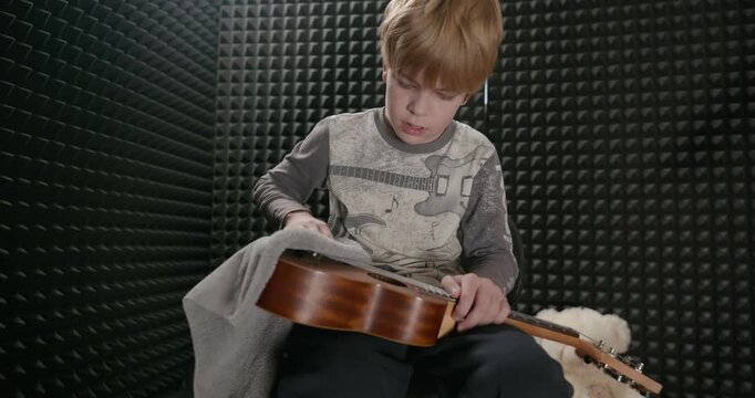 Boy Wipes Dust Cleaning Ukulele Instrument in Home Studio. 4K 10-bit