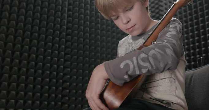 Boy Wipes Dust Cleaning Ukulele Instrument in Home Studio. 4K 10-bit