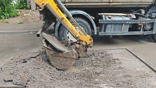 Close-up of a hydraulic excavator bucket scooping broken asphalt during road repair works.