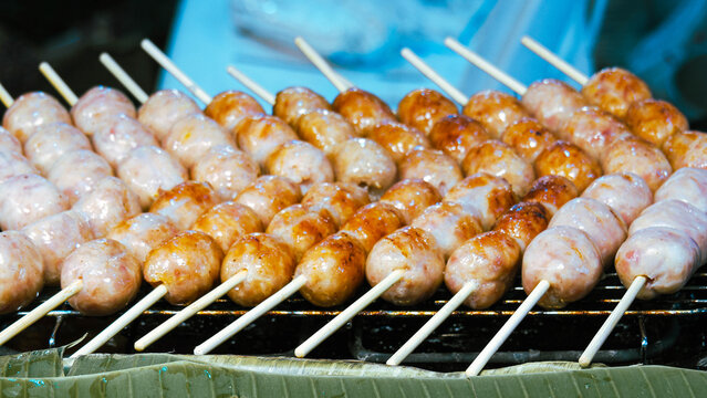 Row of hot glossy Thai sour sausages on wooden sticks, famous northeastern Thailand street food appetizer backdrop.