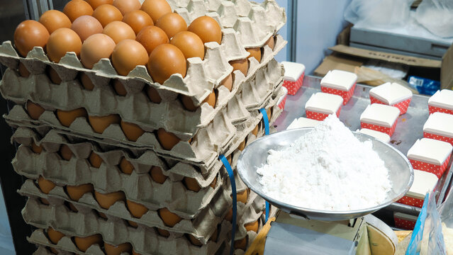 Baking ingredients preparation with stack of chicken egg trays and white flour on a weighing scale.