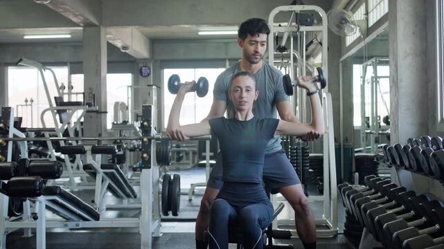 Personal trainer helping woman with dumbbell workout in contemporary fitness center environment