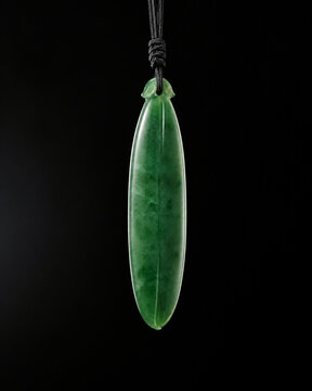 A slender green jade pendant shaped like a silique on a dark background.