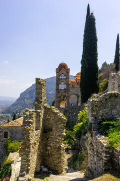 Ruins of Mystras, Greece, with a Byzantine church tower and cypress trees under a clear blue sky.