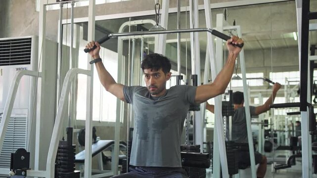 Dedicated young man performing strength exercises using a cable pulley machine in a modern gym setting