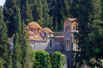 The Monastery of Hosios Loukas, a Byzantine church with multiple domes and arched windows, nestled among lush green trees in Greece. © Nick