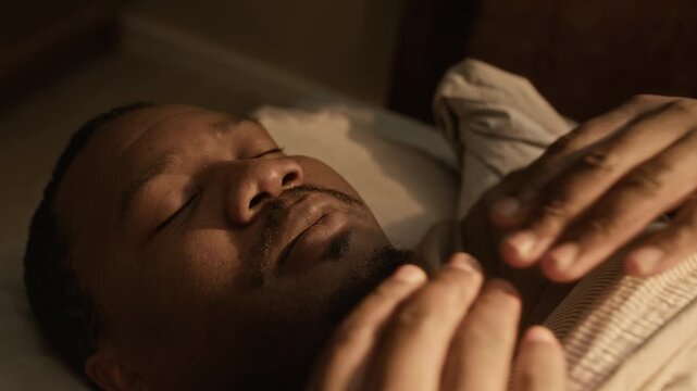Close up shot of young African American man waking up in bed, rubbing face and going back to sleep. Footage is perfect for sleep disorder awareness or mental health campaigns