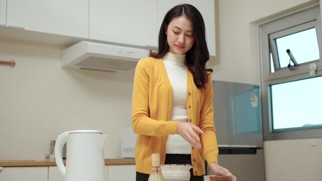 Pretty young woman making traditional green tea matcha using bamboo natural whisk mixing beverage for healthy drink with antioxidant nutrition in wellness routine and modern healthy lifestyle.
