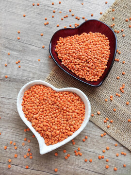 Red lentils in a decorative heart-shaped bowl on a brown wooden background. Healthy plant-based food, nutritious ingredient, top view, soft lighting.