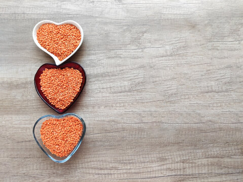 Red lentils in a decorative heart-shaped bowl on a brown wooden background. Healthy plant-based food, nutritious ingredient, top view, soft lighting.