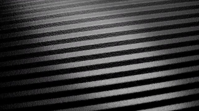 Striped ribbed texture slow rotation. Close-up of black and gray parallel ridges with textured surface. Smooth continuous rotation reveals shifting light and shadow across the linear pattern.