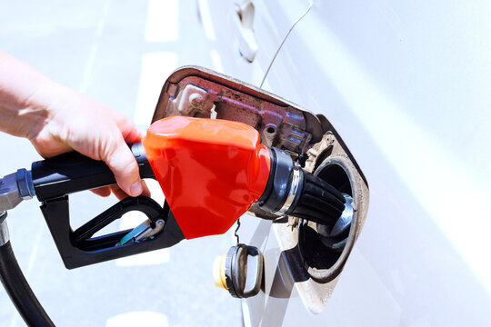 Person is fueling car at gas station gas nozzle is being inserted into tank.