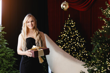 Fototapeta premium Happy Woman with makeup holding gift amidst festive christmas trees and holiday decor, hair styling