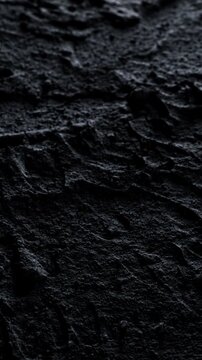 Dark cracked rough texture slow pan. Close-up of deep black rough surface with irregular cracks and relief. Smooth linear camera movement reveals shifting light and shadow across the textured details.