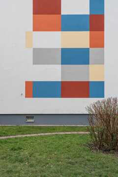 Minimalist architectural composition of an outdoor building wall decorated with a large geometric pattern of multicolored painted squares and rectangles.