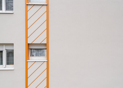 Architectural detail of a clean white concrete residential building facade featuring windows and a distinctive bright orange geometric accent vertical stripe with.