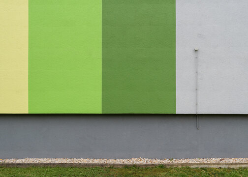 Minimalist abstract view of a plastered residential building wall painted in distinctive vertical shades of yellow, light green, dark green, and white.