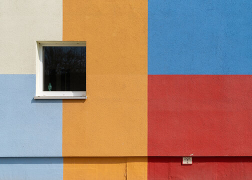 Frame of a stucco building facade combining a single window with solid painted blocks of blue, red, orange, and white.